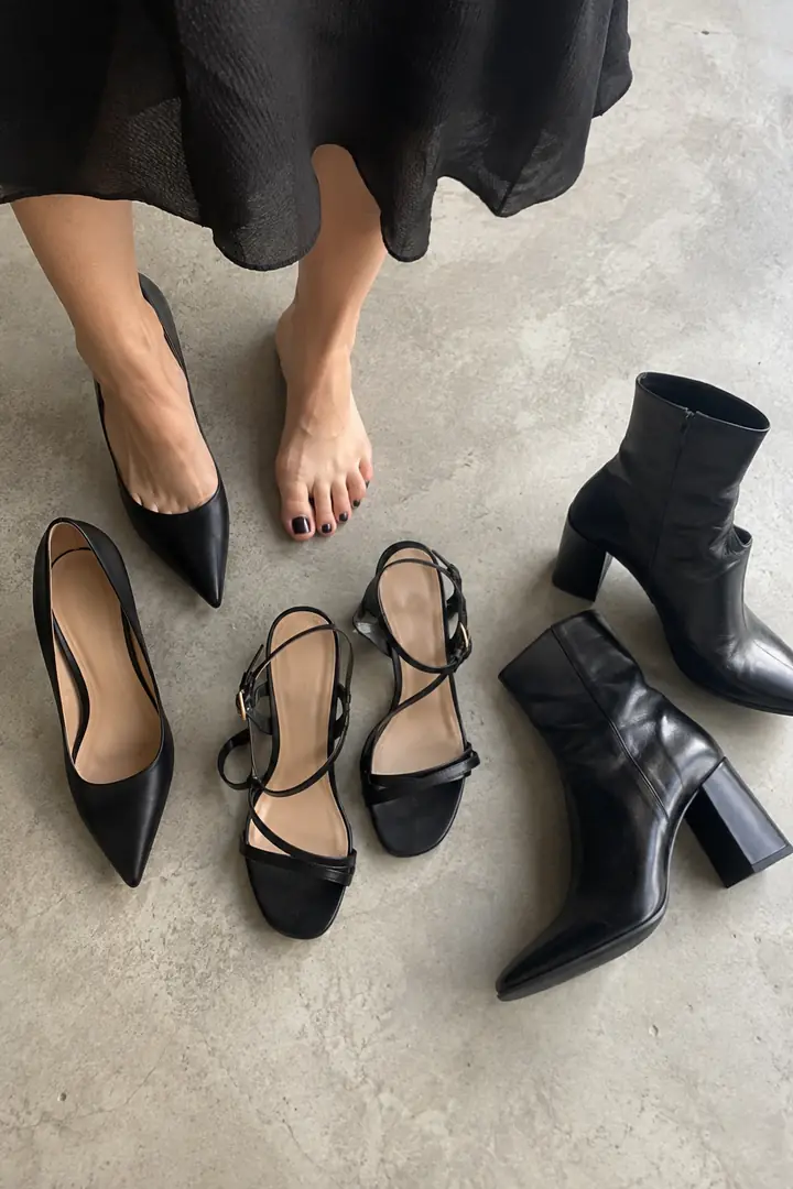Flat lay of a black dress hem with a pointed pump, a strappy sandal and an ankle boot